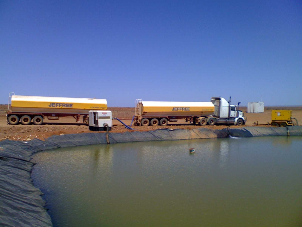 Two tanker trucks alongside a water reservoir in a desert landscape.— Ts Jeffree Contractors in Tennant Creek, NT