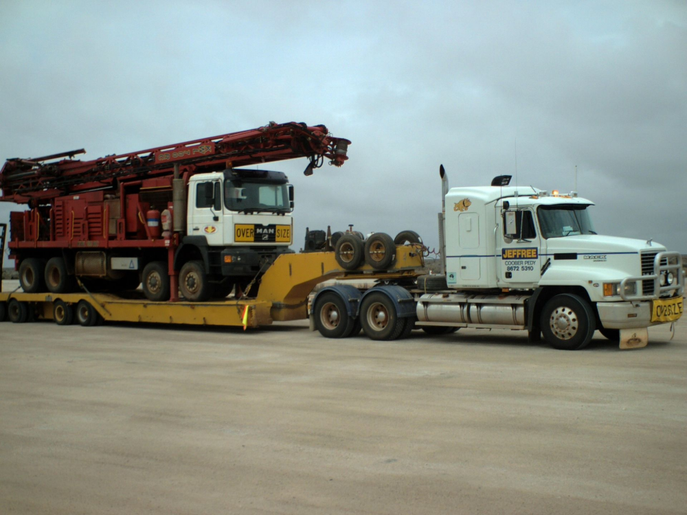 Truck transporting a drilling rig on a flatbed trailer, overcast sky.— Ts Jeffree Contractors in Mount Isa, QLD