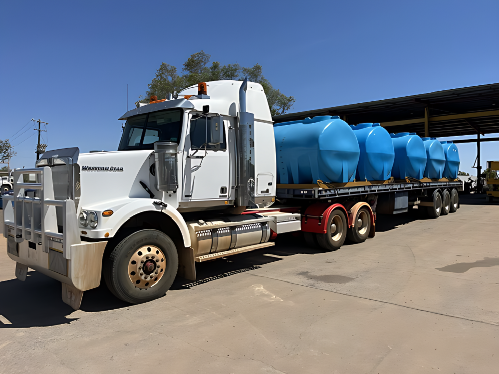 White semi truck hauling blue tank containers on a flatbed trailer in an industrial yard — Ts Jeffree Contractors in Cloncurry, QLD