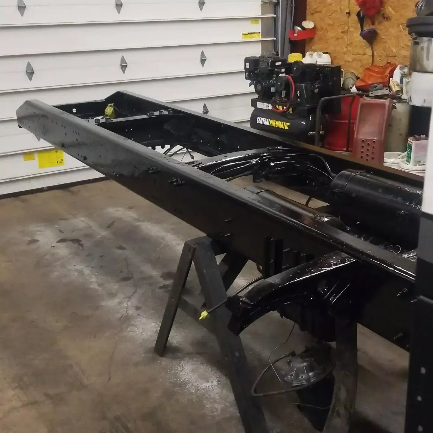 Black truck chassis on sawhorses inside a garage, waiting for restoration.