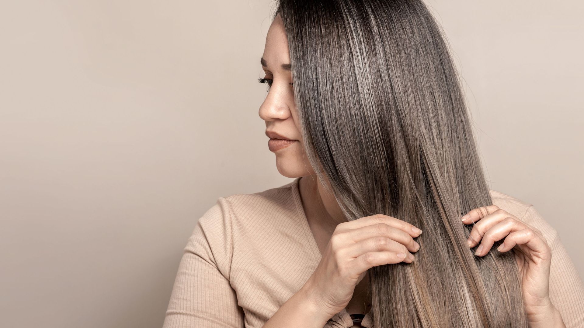 A woman is brushing her long hair against a beige background.