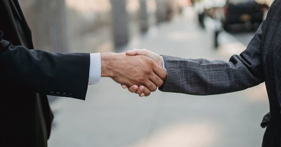 Two men in suits are shaking hands on a city street.