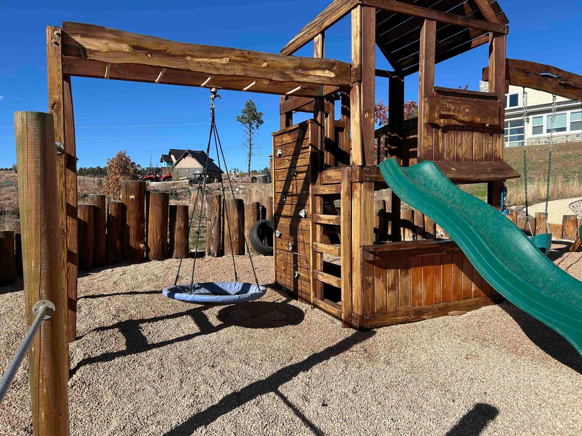 Wooden playground with a swing set and slide on gravel.