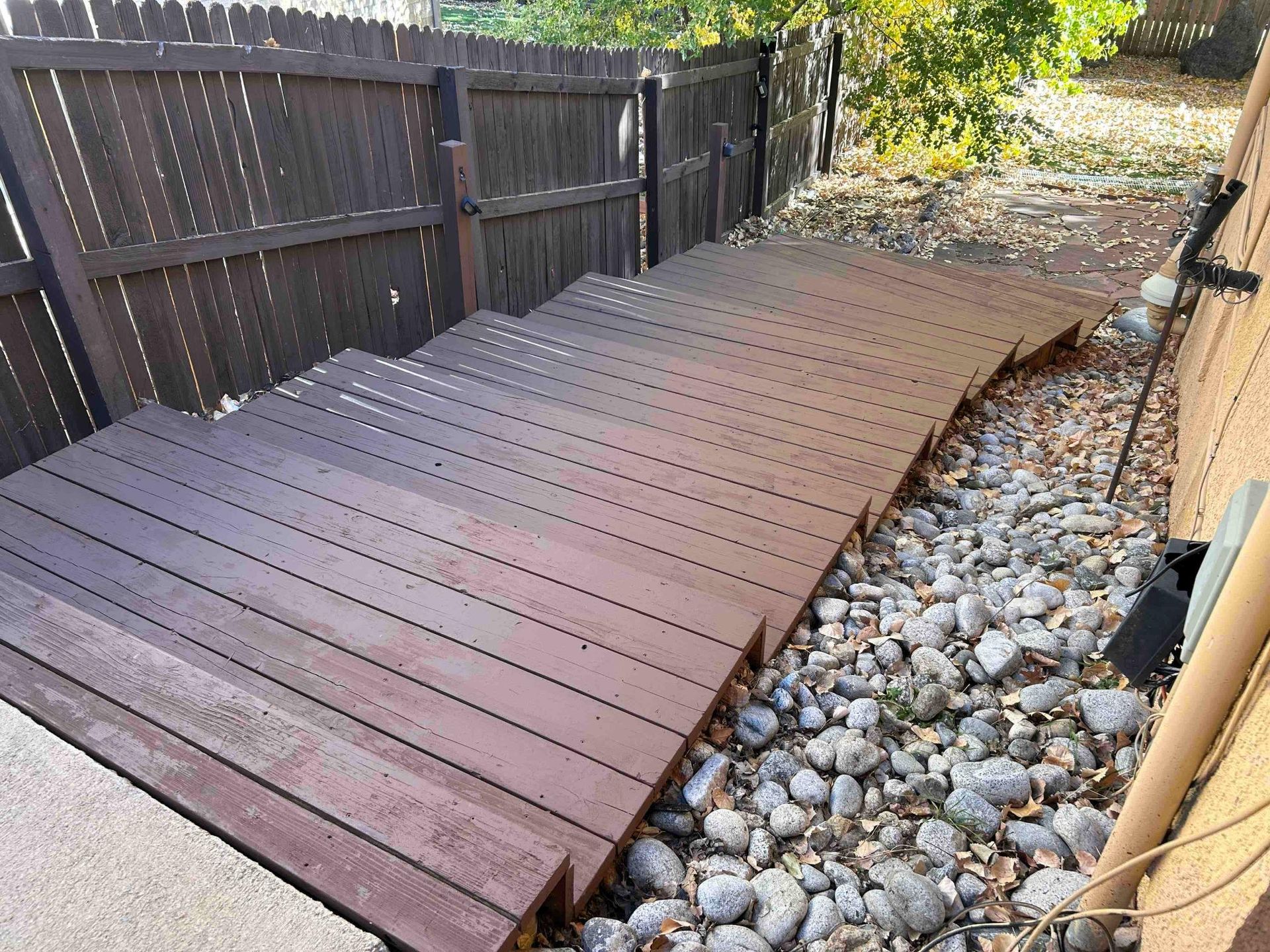 Wooden steps and ramp alongside a building with a rock bed, leading to a fenced area.