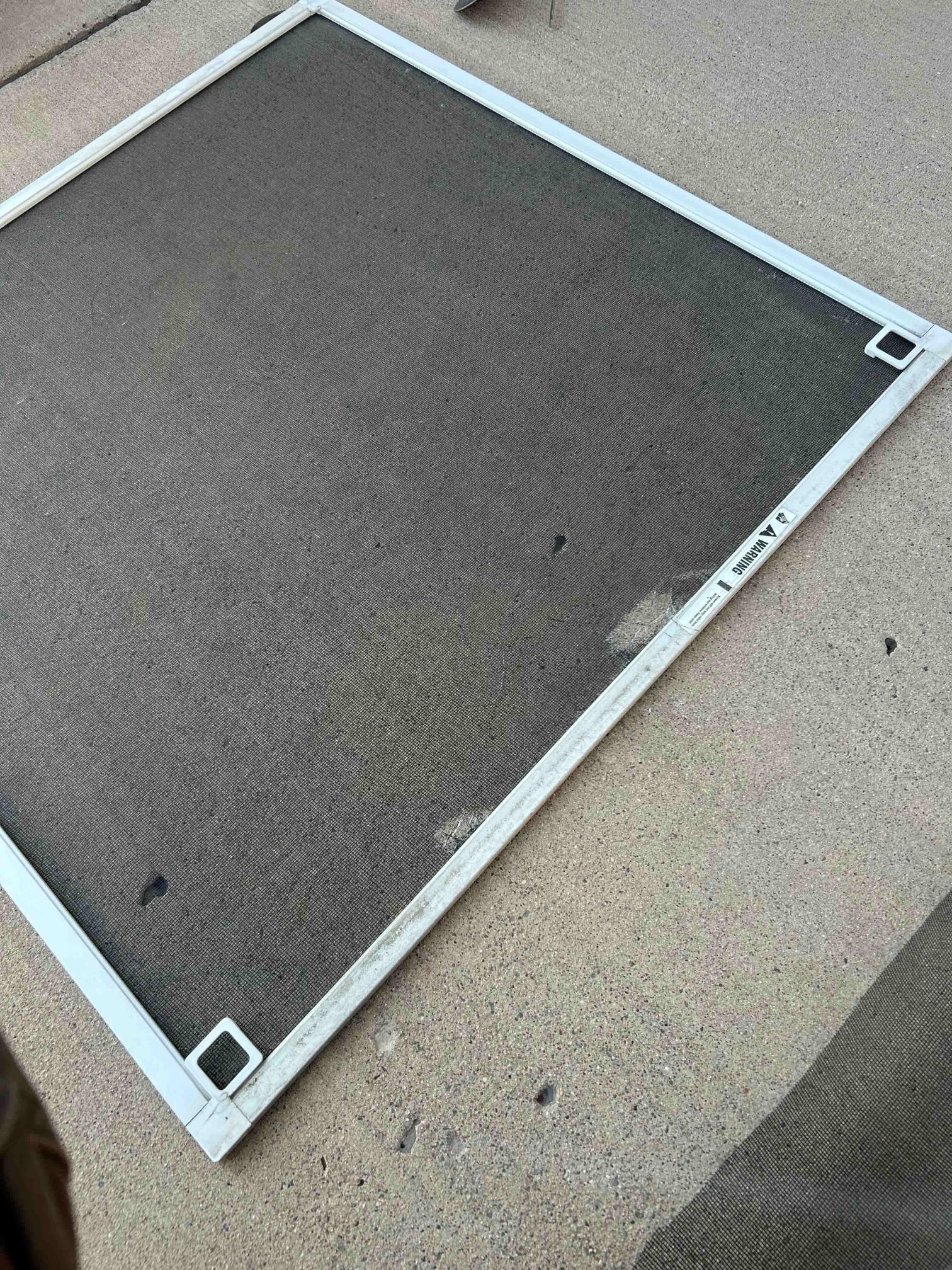 White-framed window screen with dark mesh, resting on a concrete surface.