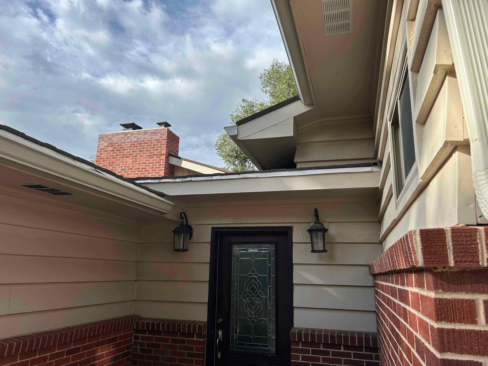 Exterior view of a home with a red brick facade, door, chimney, and cloudy sky.