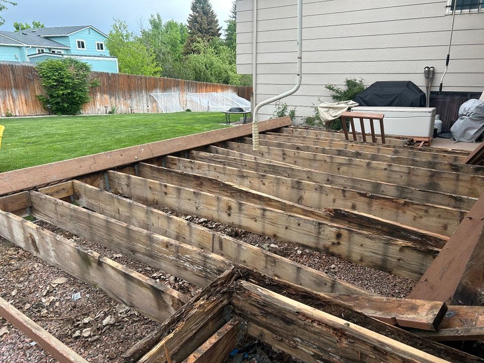 Partially dismantled wooden deck in backyard; framing exposed.