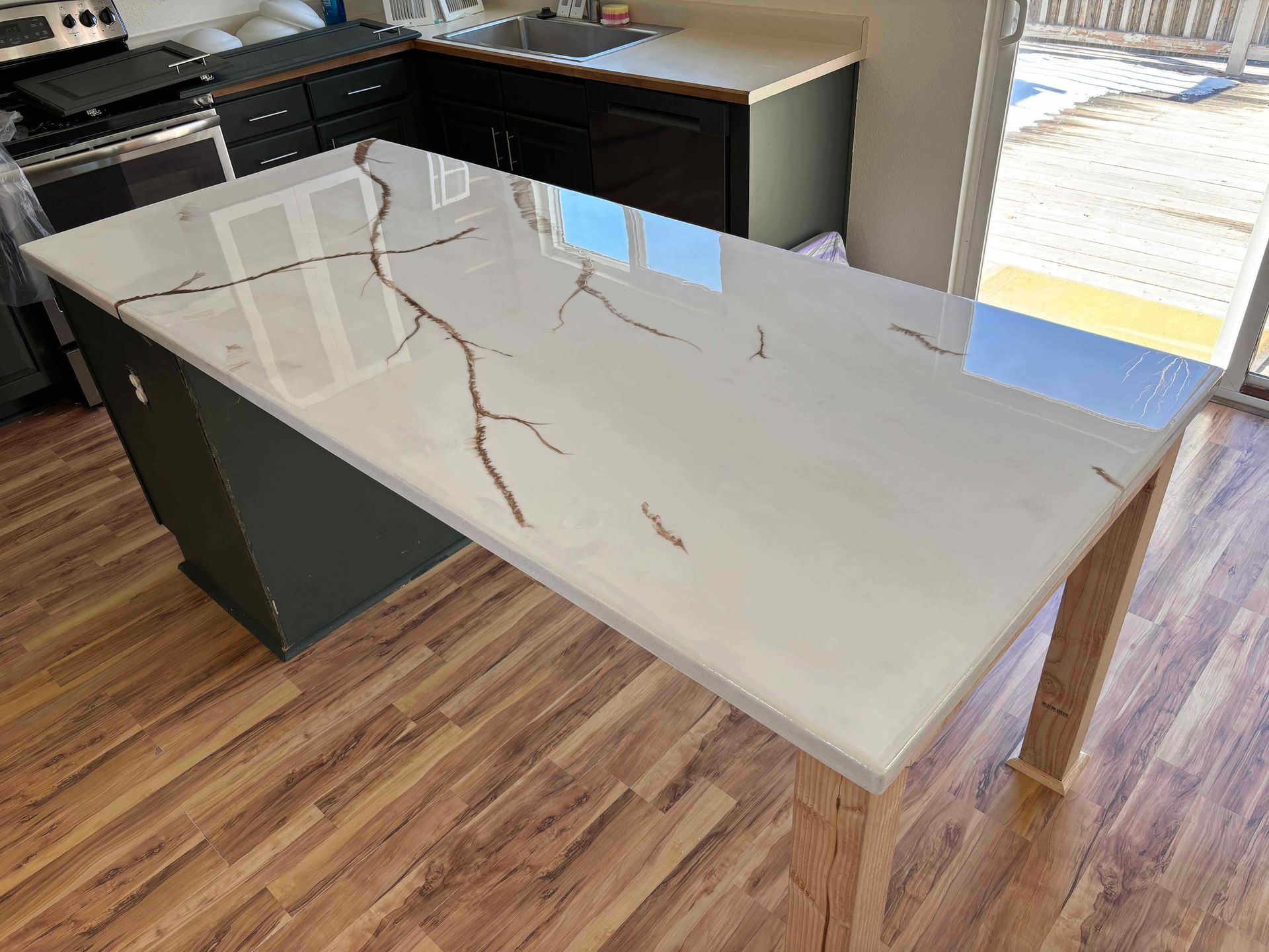 Kitchen island with white countertop featuring brown veining, gray base, wood legs, and wood flooring.