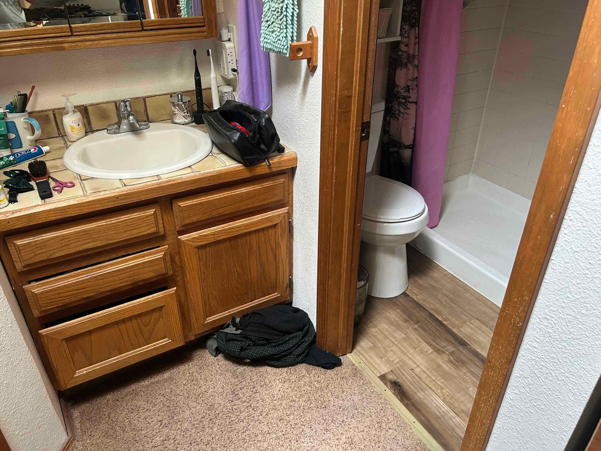 Bathroom with sink, toilet, and shower. Wooden cabinets and door frames. Pink shower curtain.