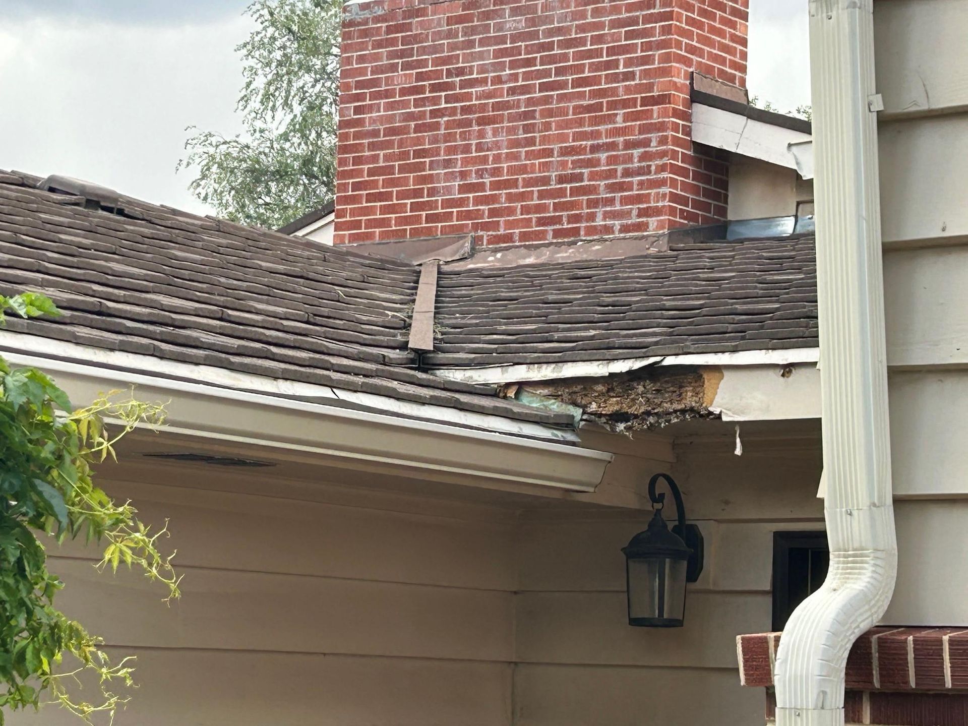 Damaged roof with missing shingles, near a brick chimney, and a white gutter.