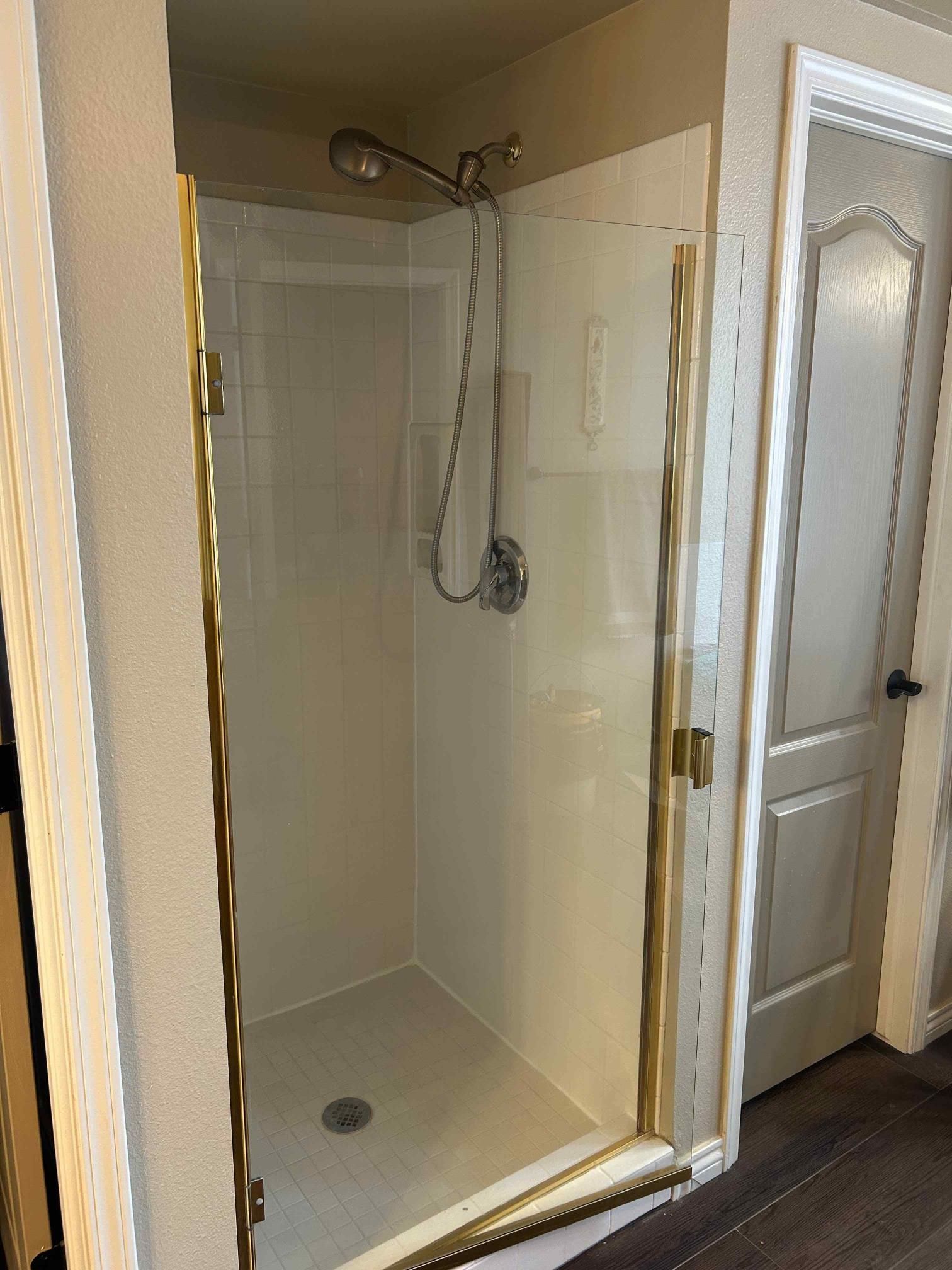 Shower with gold-colored trim and a glass door. Adjacent to a closed, light-colored door.