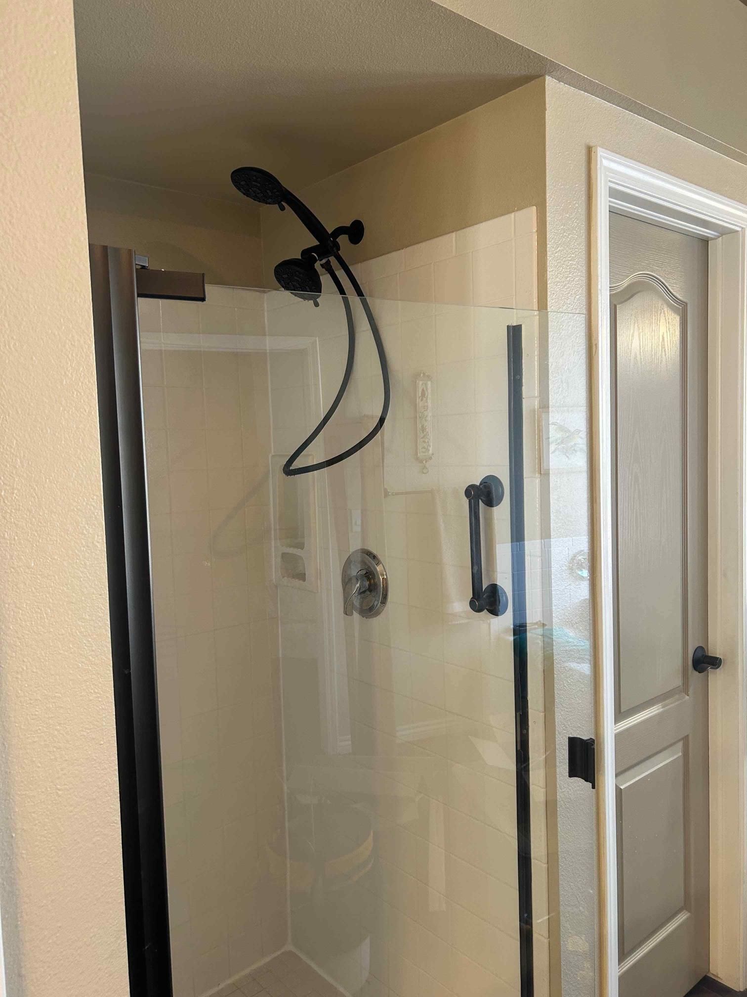 Shower with black frame and hardware, next to a closed door, in a bathroom.
