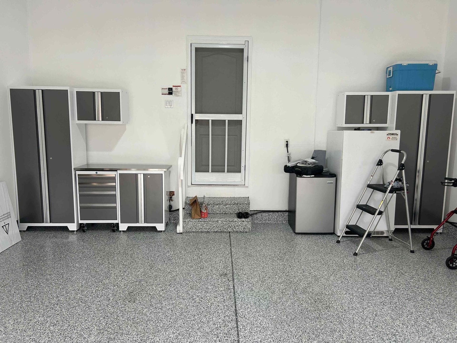 Garage with gray cabinets, white walls, speckled floor, door, and equipment.