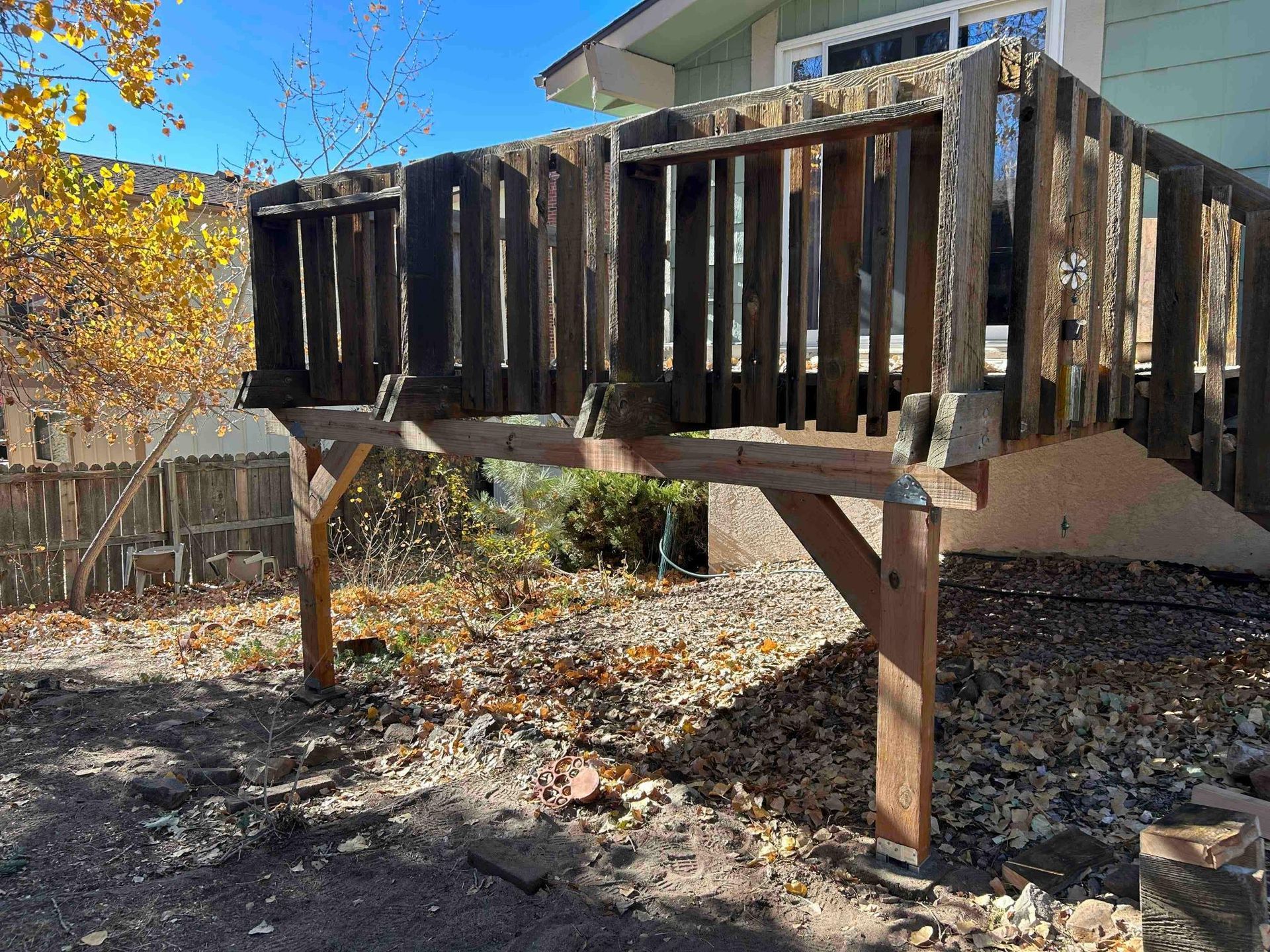 Old weathered wooden deck on supports in a yard with leaves.