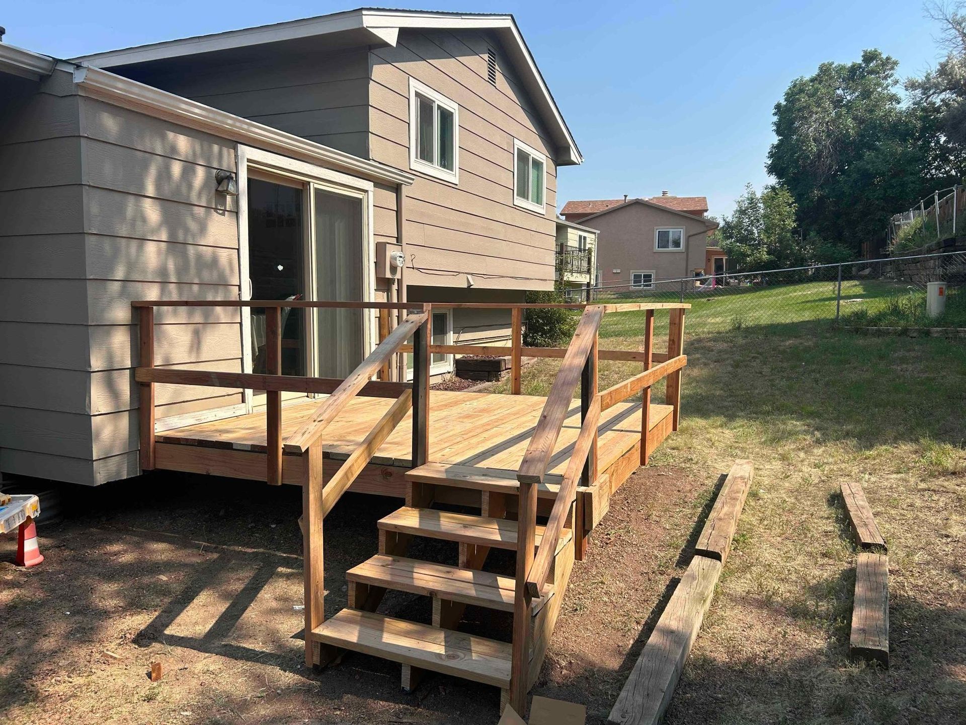Newly built wooden deck with stairs attached to a beige house, surrounded by grass and a yard.