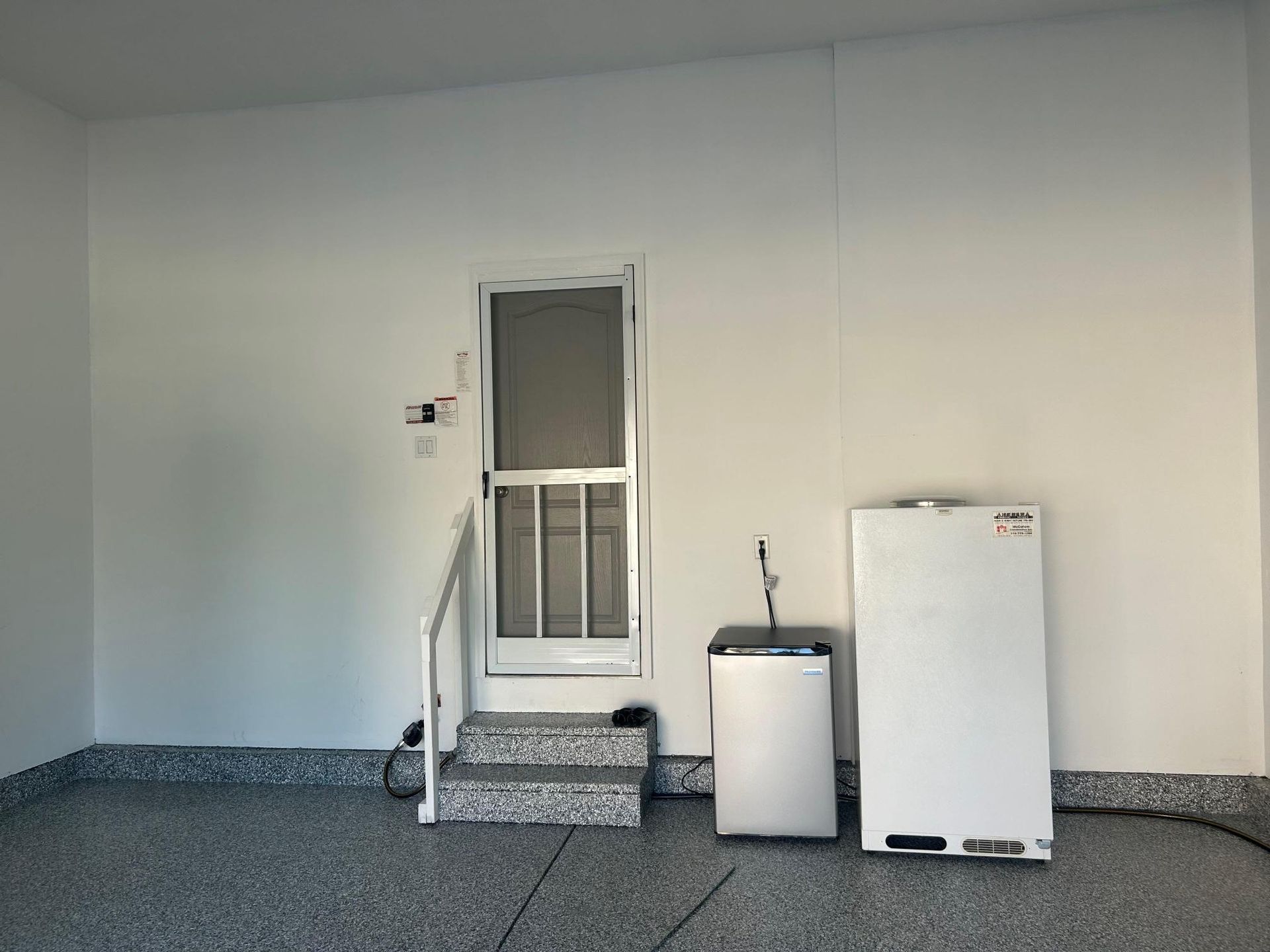 A white door with steps, a metal cabinet, and a white panel in a garage with speckled flooring.