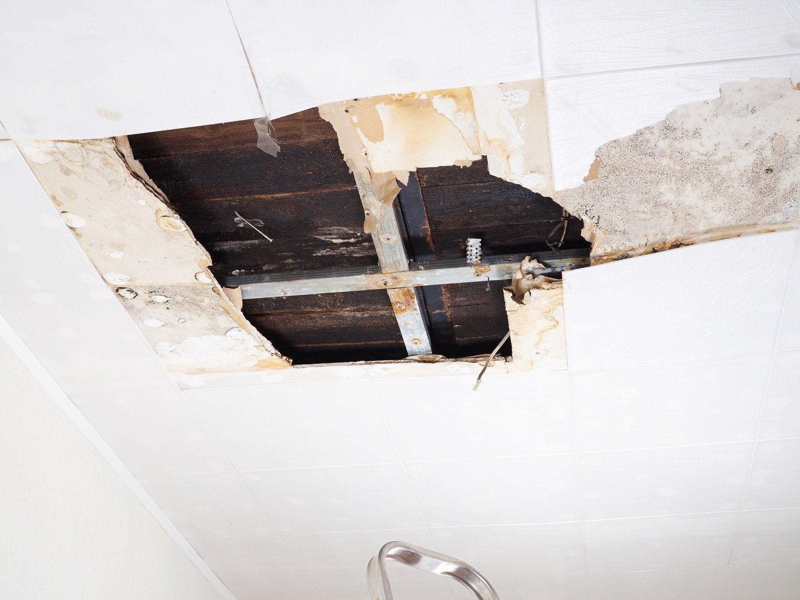 Damaged ceiling with a large hole, revealing wood beams, metal support, and water stains.