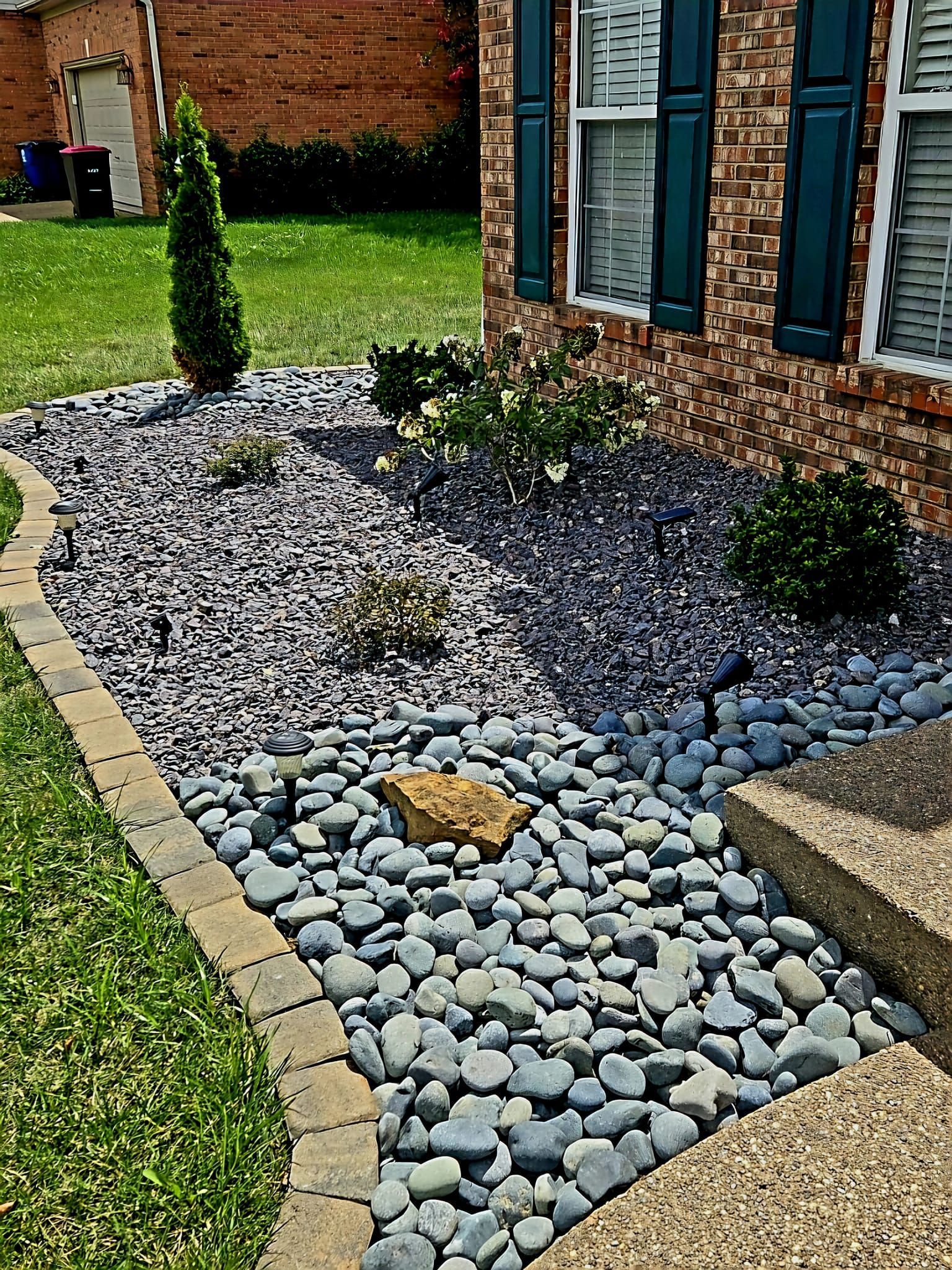 A garden with rocks and plants in front of a brick house.