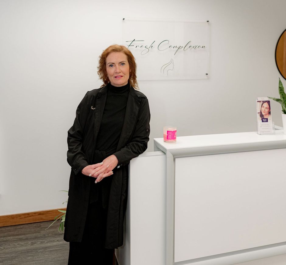 Woman in black coat standing by a white reception desk in a modern lobby.
