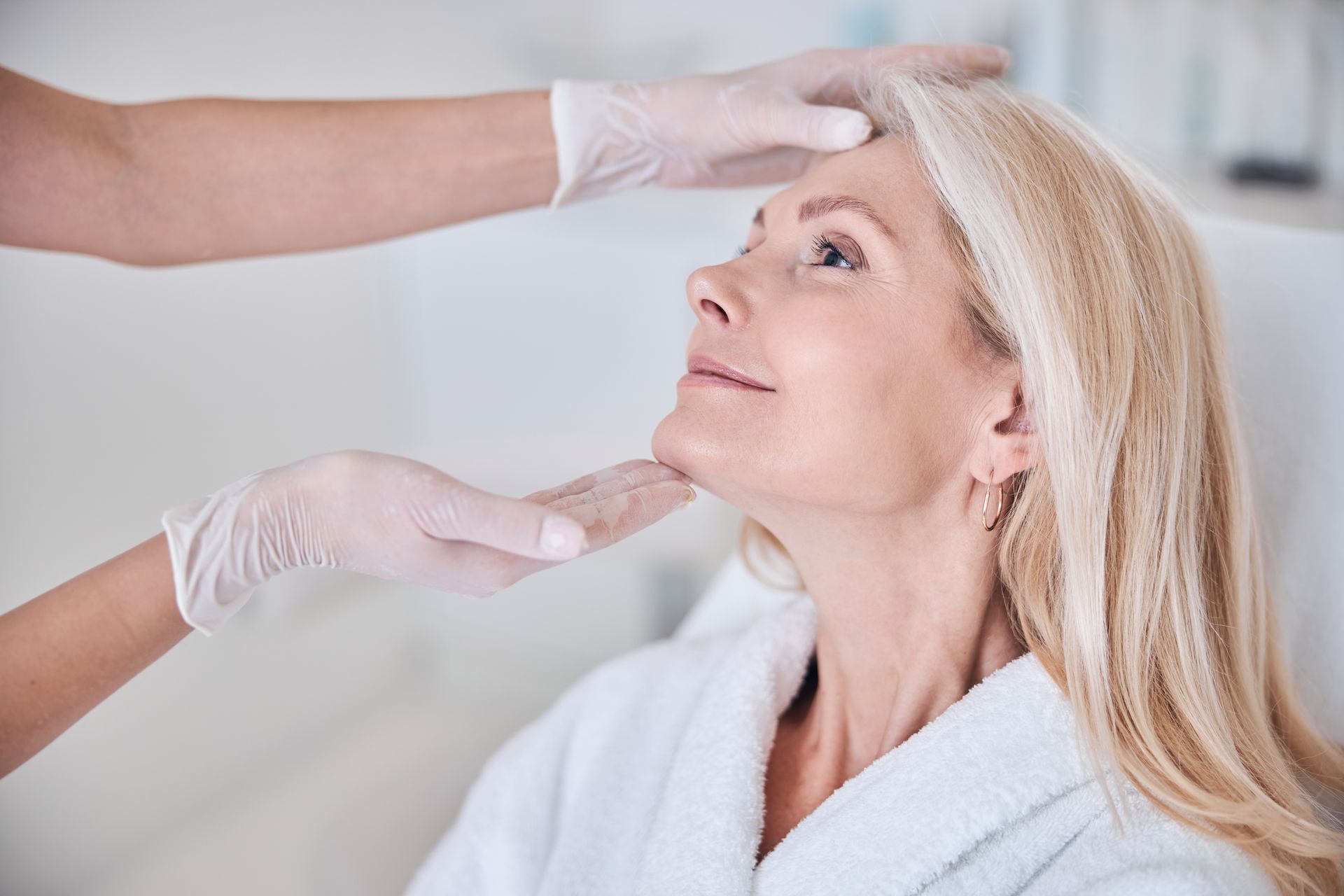 Gloved clinician applying eyebrow treatment to a woman reclining in a spa robe