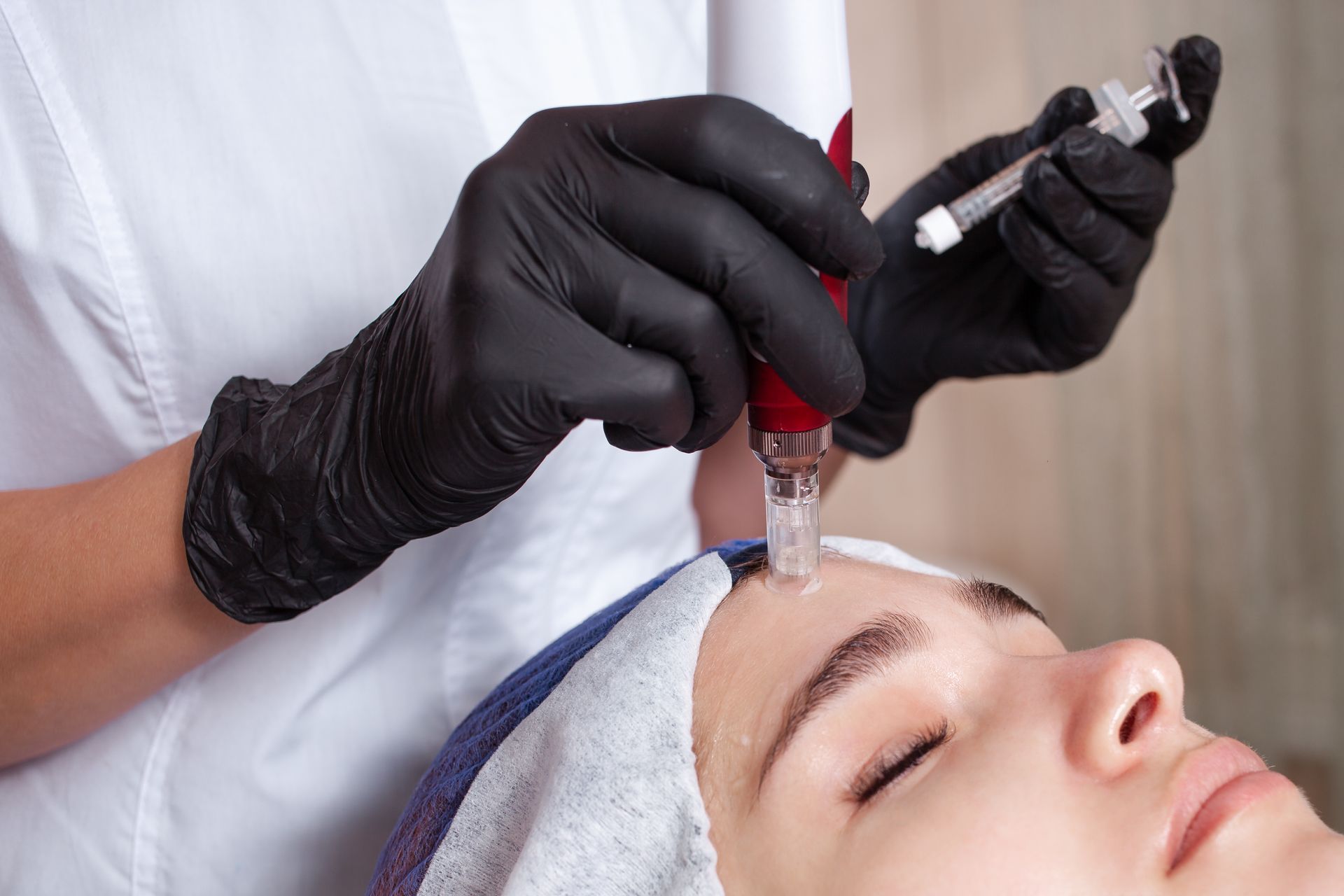 Gloved hands performing a facial injection on a reclining client with a syringe and red device