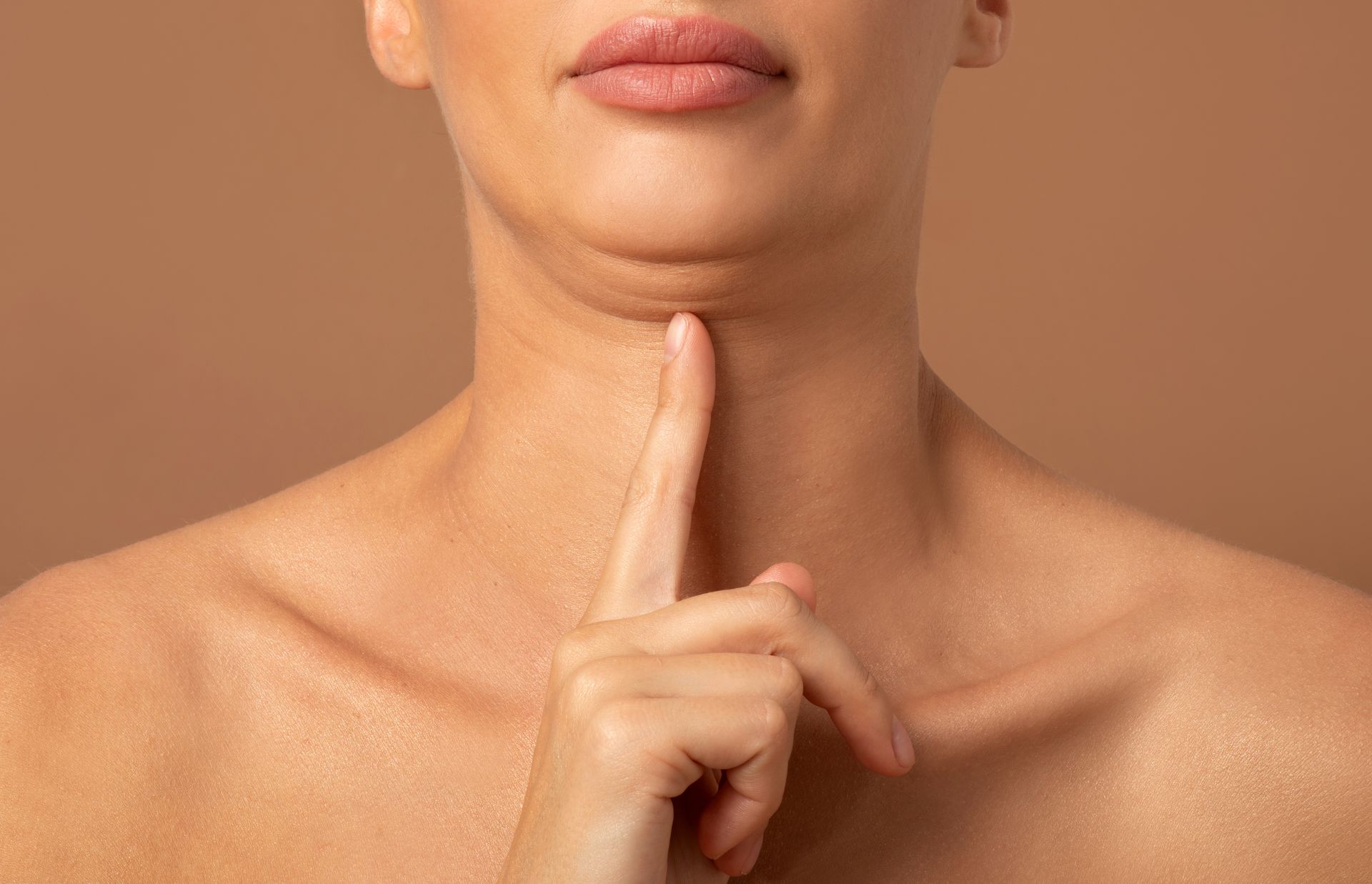 Person holding a finger to the chin against a plain tan background