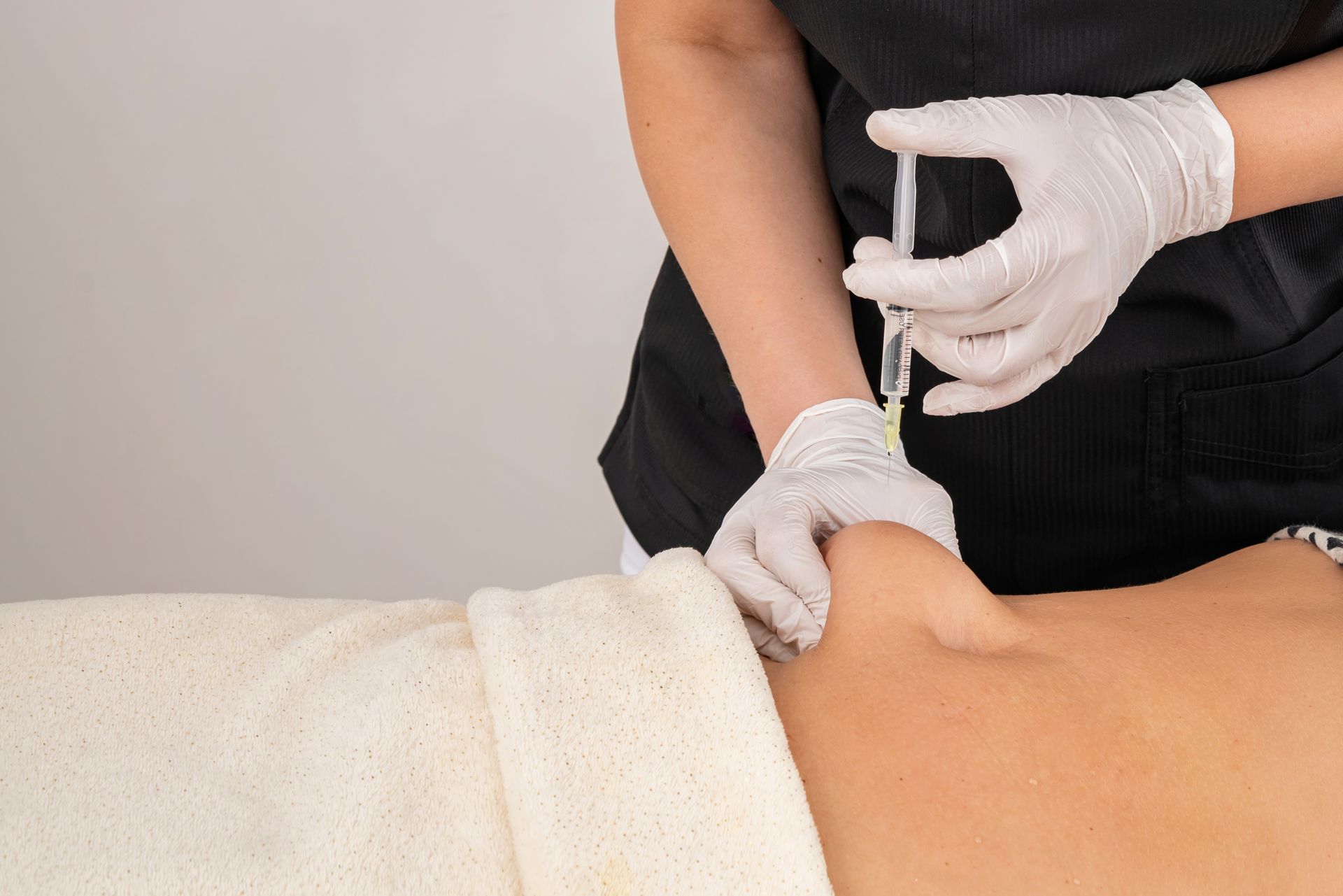 Gloved practitioner injecting a patient’s lower back during a medical procedure