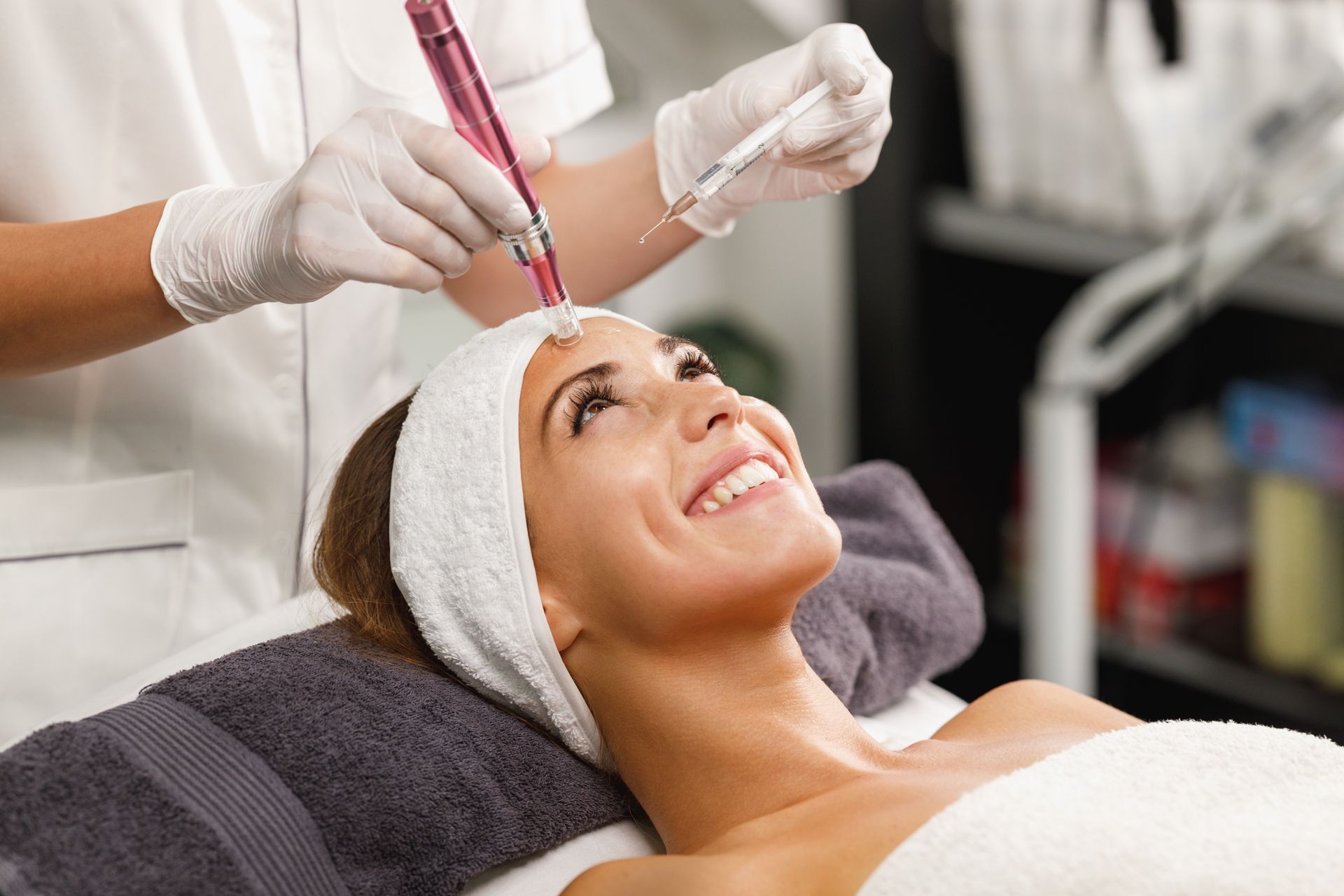 A smiling person receives a professional microneedling facial treatment from a provider wearing white gloves.