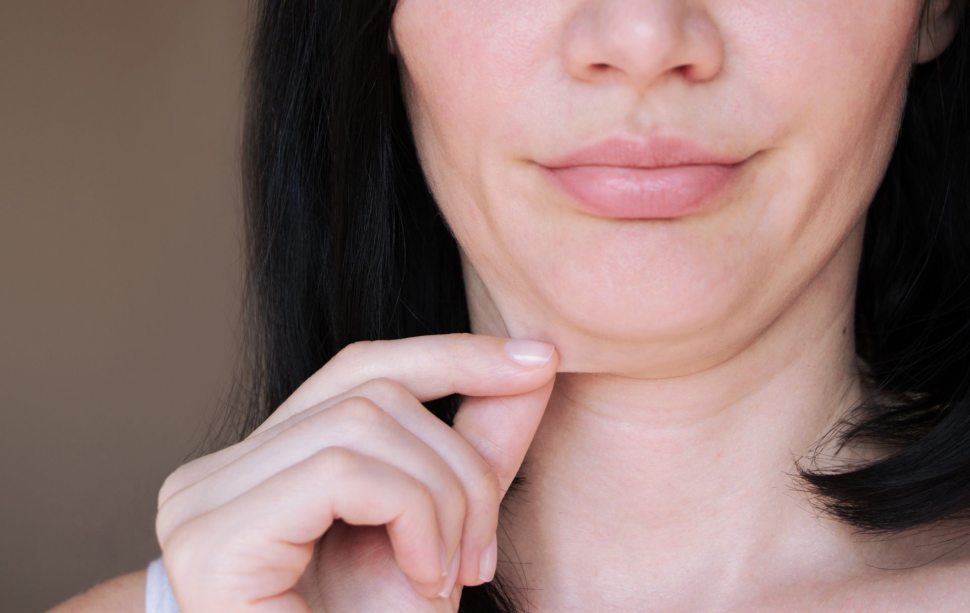 Woman pinching her double chin, smiling slightly.