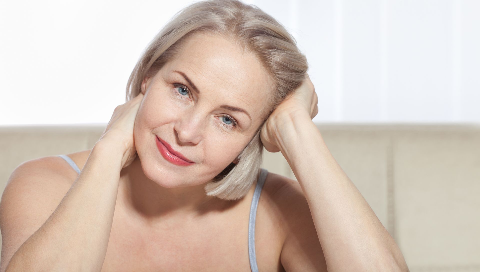 Woman with short blonde hair, resting head in hands, smiling.