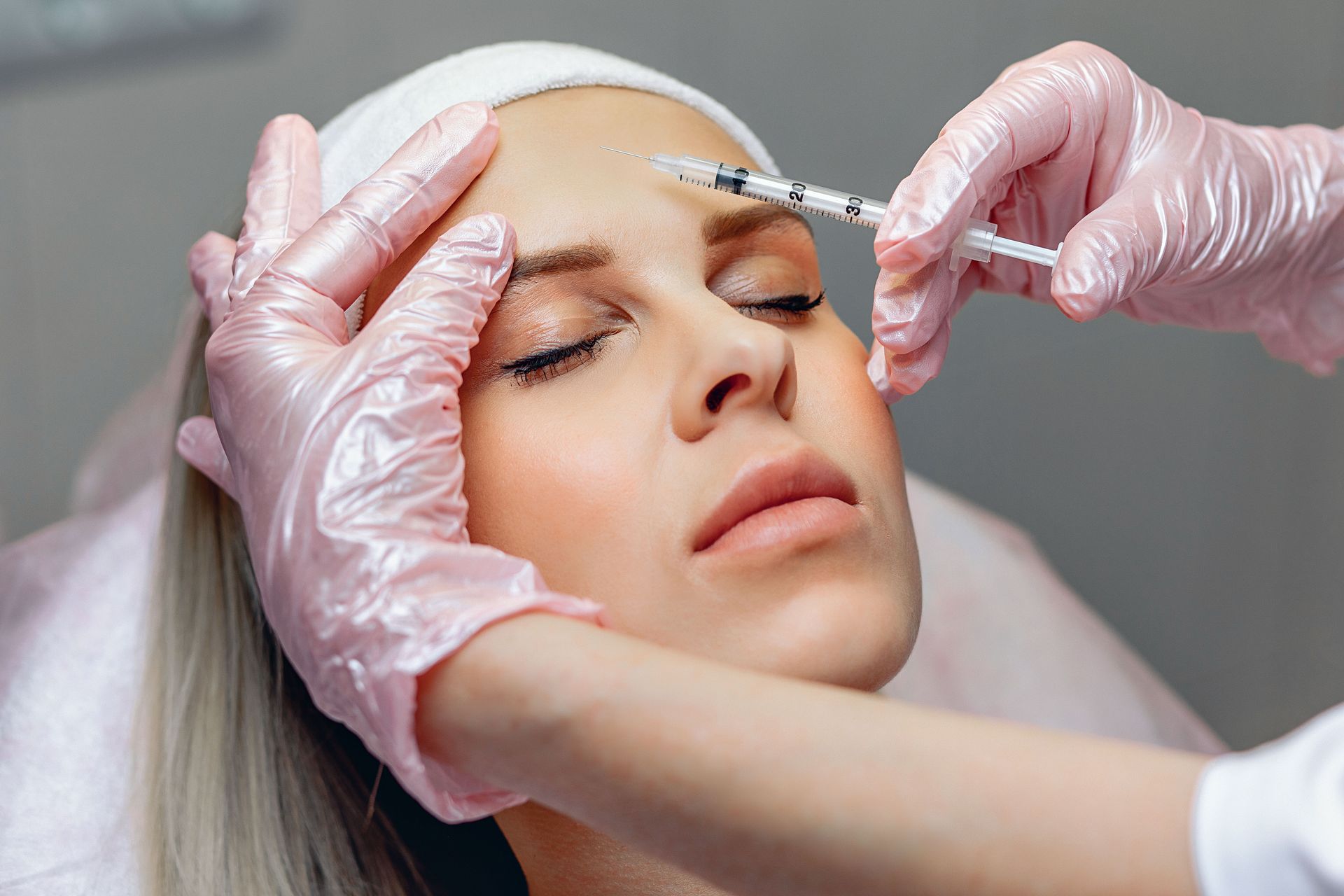 Woman receiving an injection in her forehead. Gloved hands holding a syringe in a medical setting.