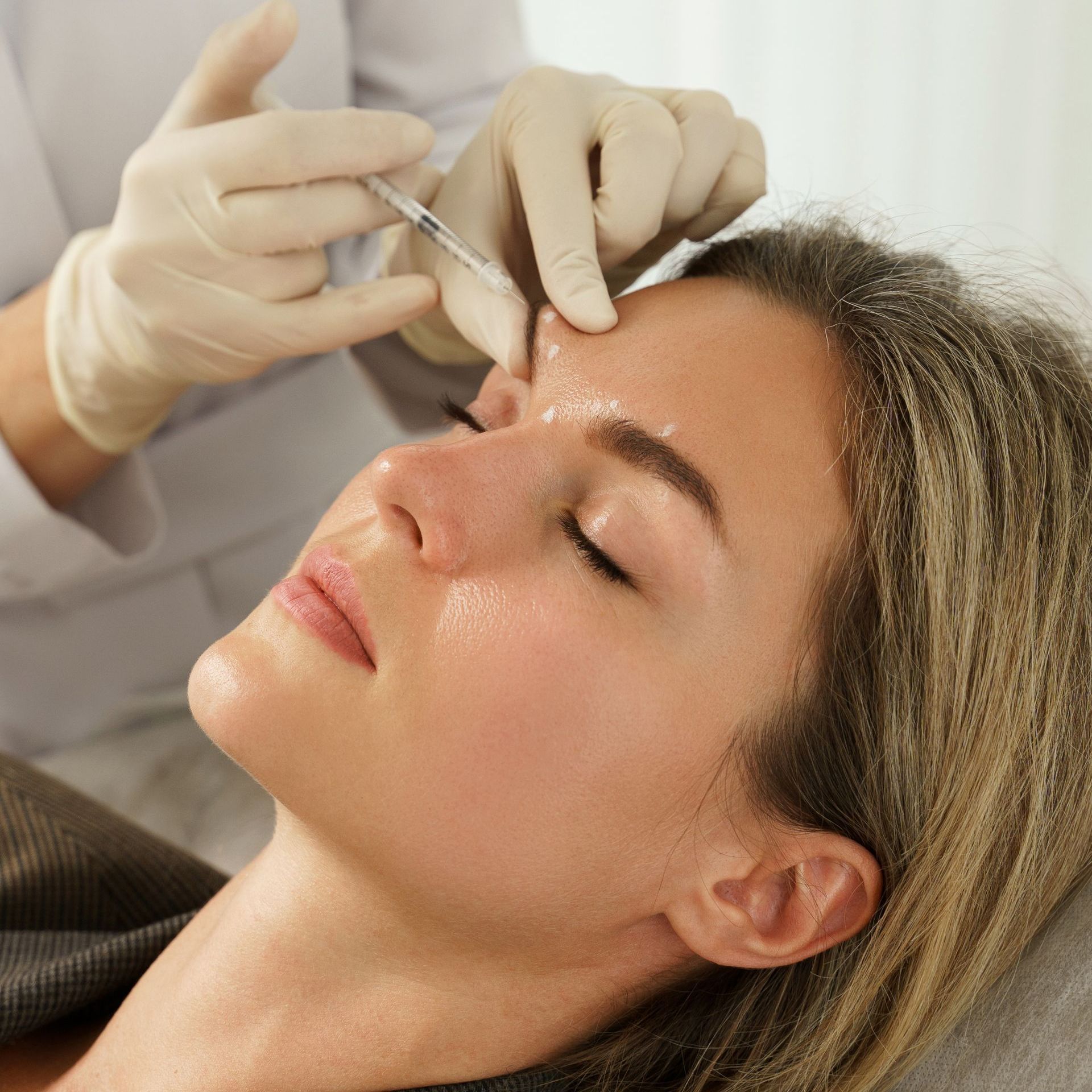 Woman receiving a facial injection on her forehead. Person wearing gloves holds a syringe.