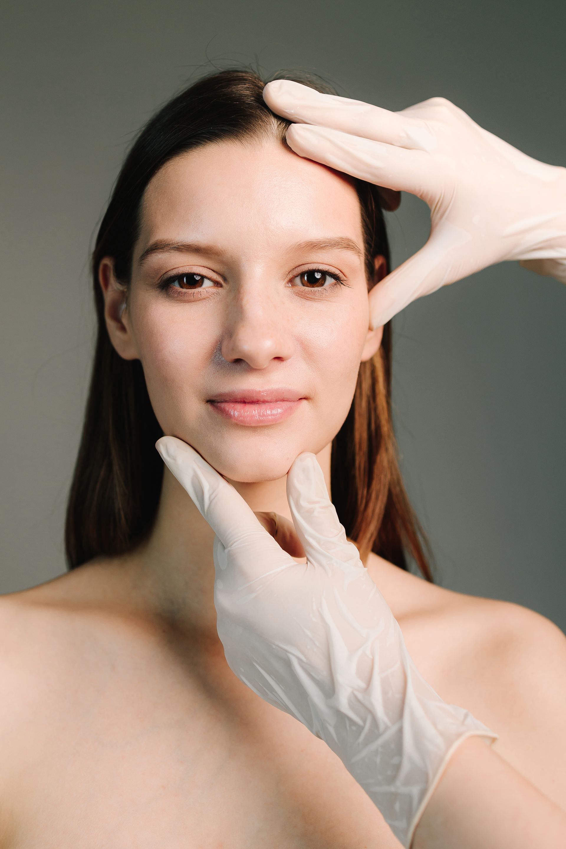 Woman's face framed by gloved hands, possibly a medical exam, neutral expression.