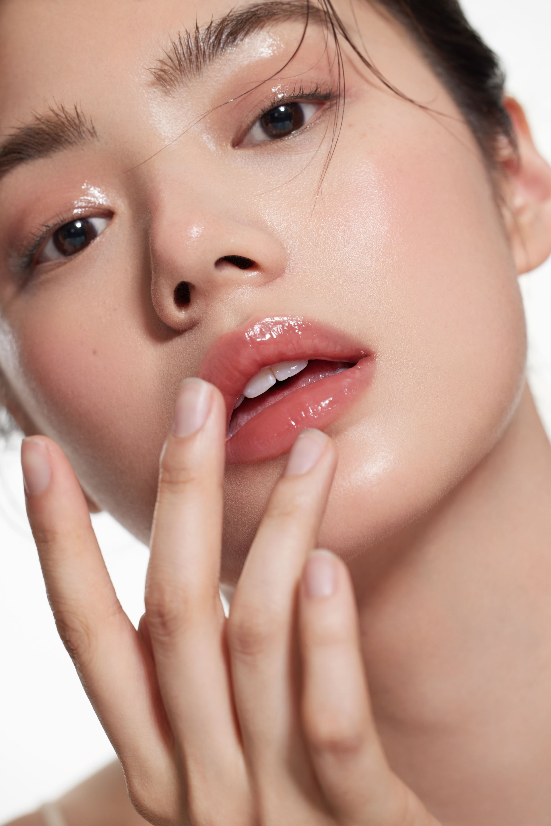 Woman with glowing skin, touching lips. Light pink makeup, glossy lips, and wet hair.