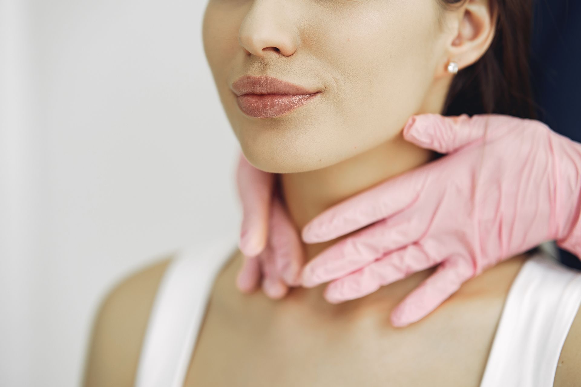 Woman's neck being examined by gloved hands, in a medical setting.