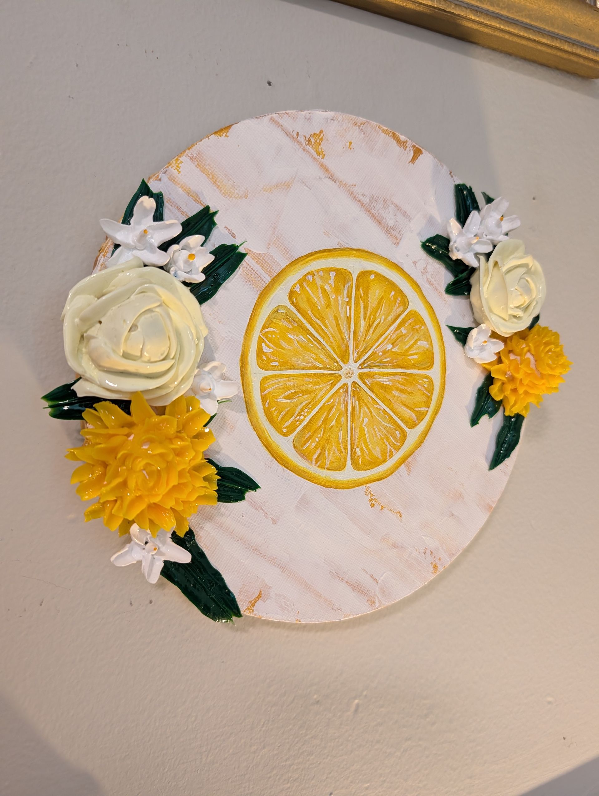 Round white wall decor with a lemon slice and yellow-white flowers on a beige wall