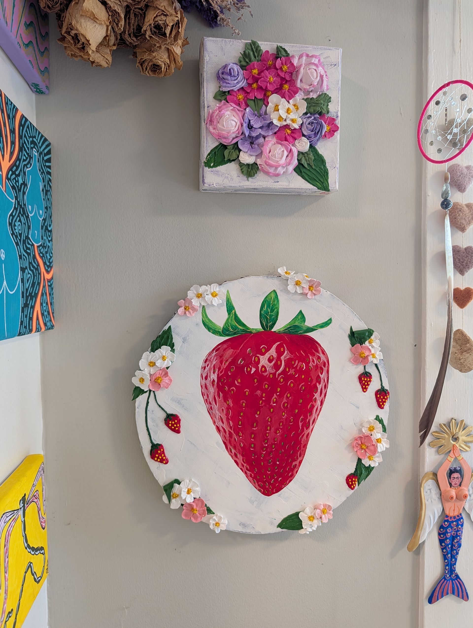Children’s artwork on a wall, including a large strawberry collage and a flower square above it
