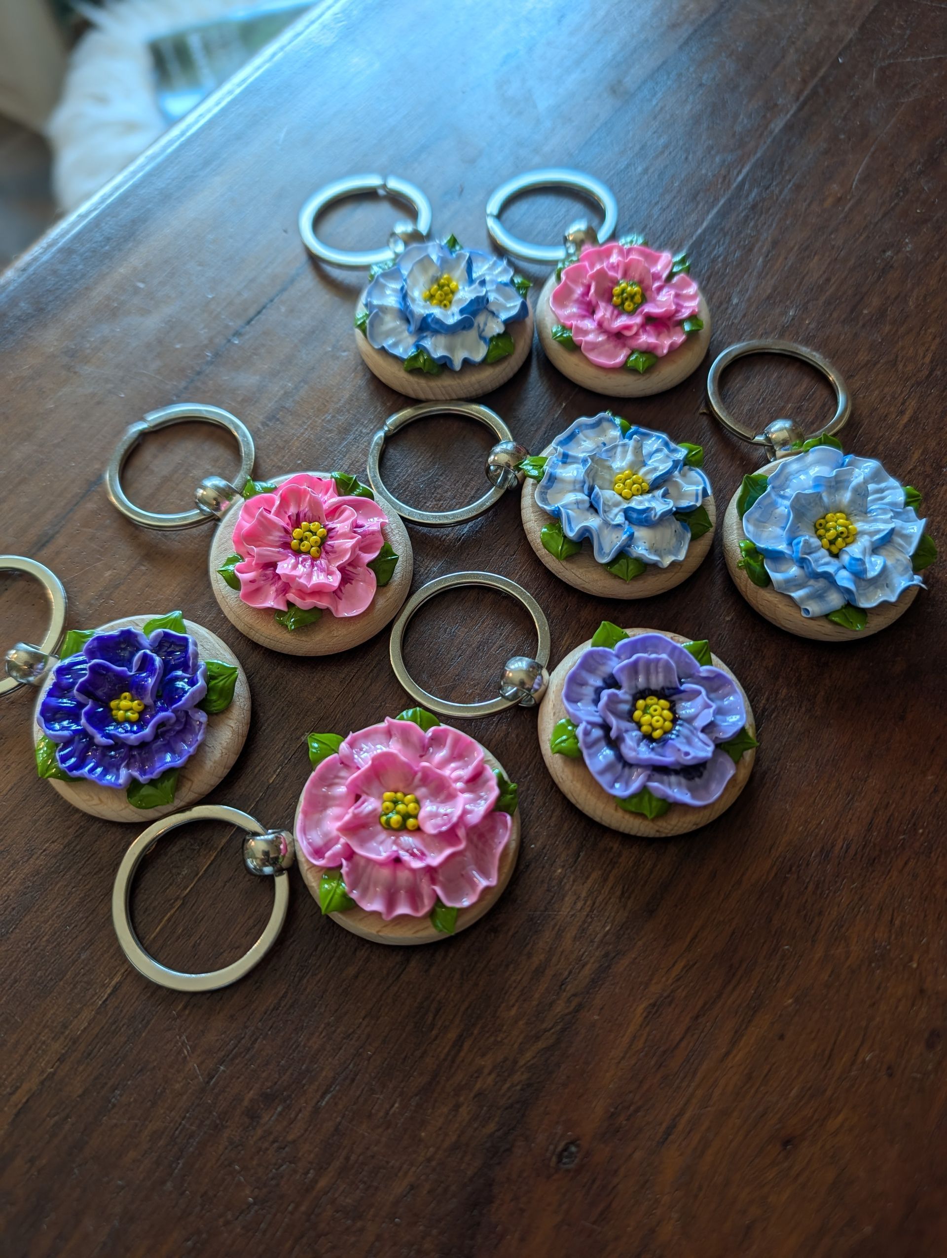 Small floral keychains with colorful resin flower designs arranged on a wooden surface