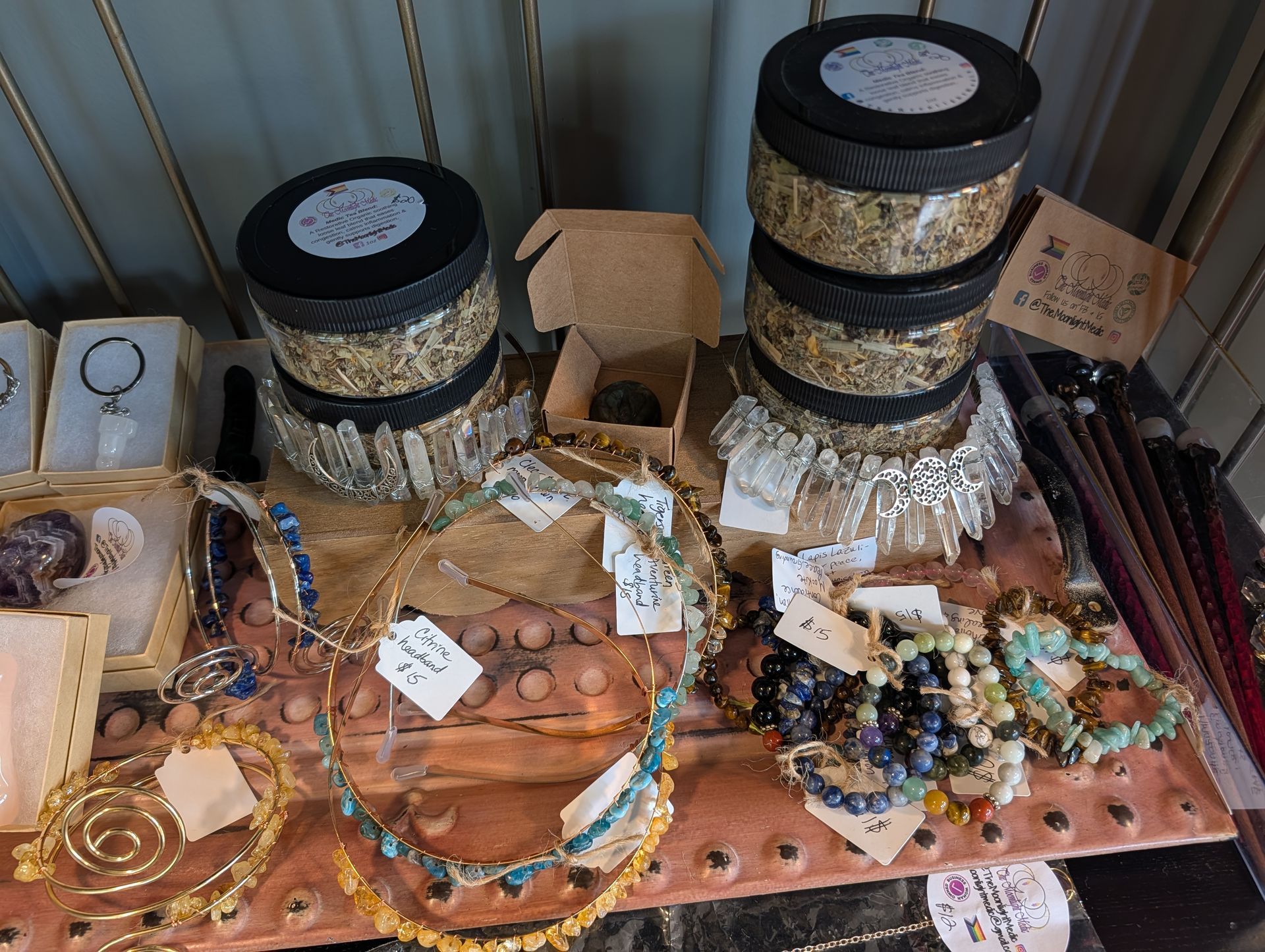 Jewelry display table with bracelets, necklaces, rings, and boxed accessories on patterned fabric background