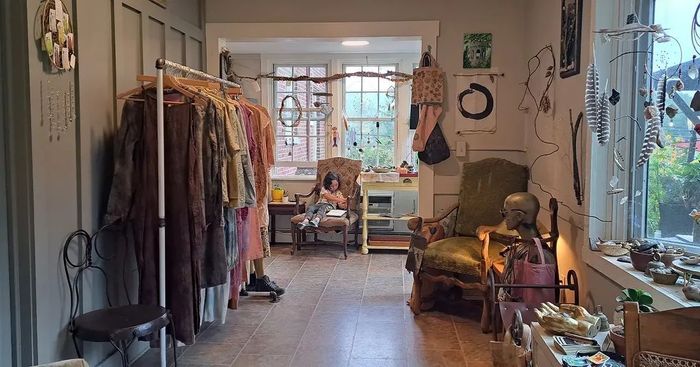 Clothing rack with various garments in a room with a window, chair, and art on the walls.