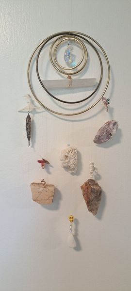 Dreamcatcher with stones and a feather on a white wall.
