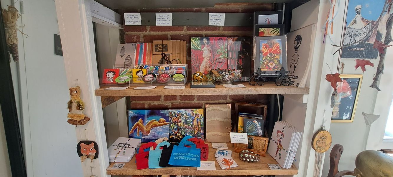 A shop display with artwork, souvenirs, and t-shirts on wooden shelves against a brick wall.