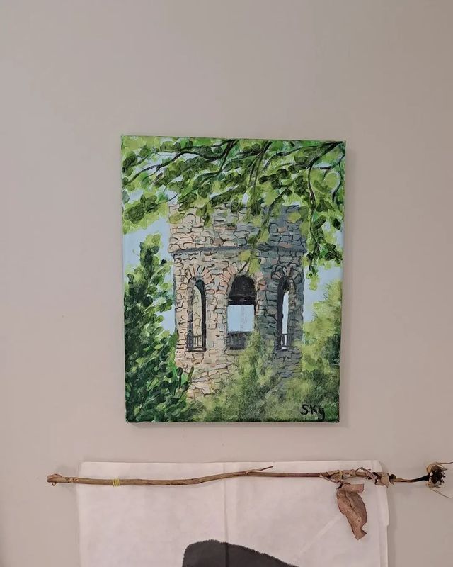 Painting of a stone tower peeking through green foliage, hanging on a wall.