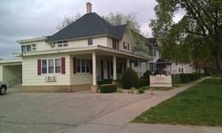 Two-story beige house with a dark roof, front porch, driveway, and lawn on a quiet suburban street