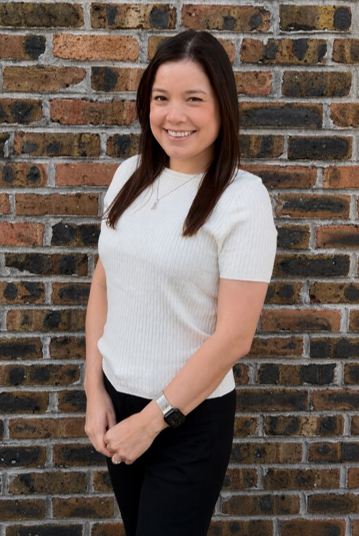 Woman with long, brown hair smiles at the camera, arms crossed, wearing a black top.