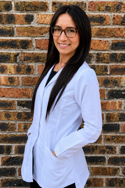 Woman with long dark hair wearing pink-rimmed glasses smiles, small nose ring, black top.