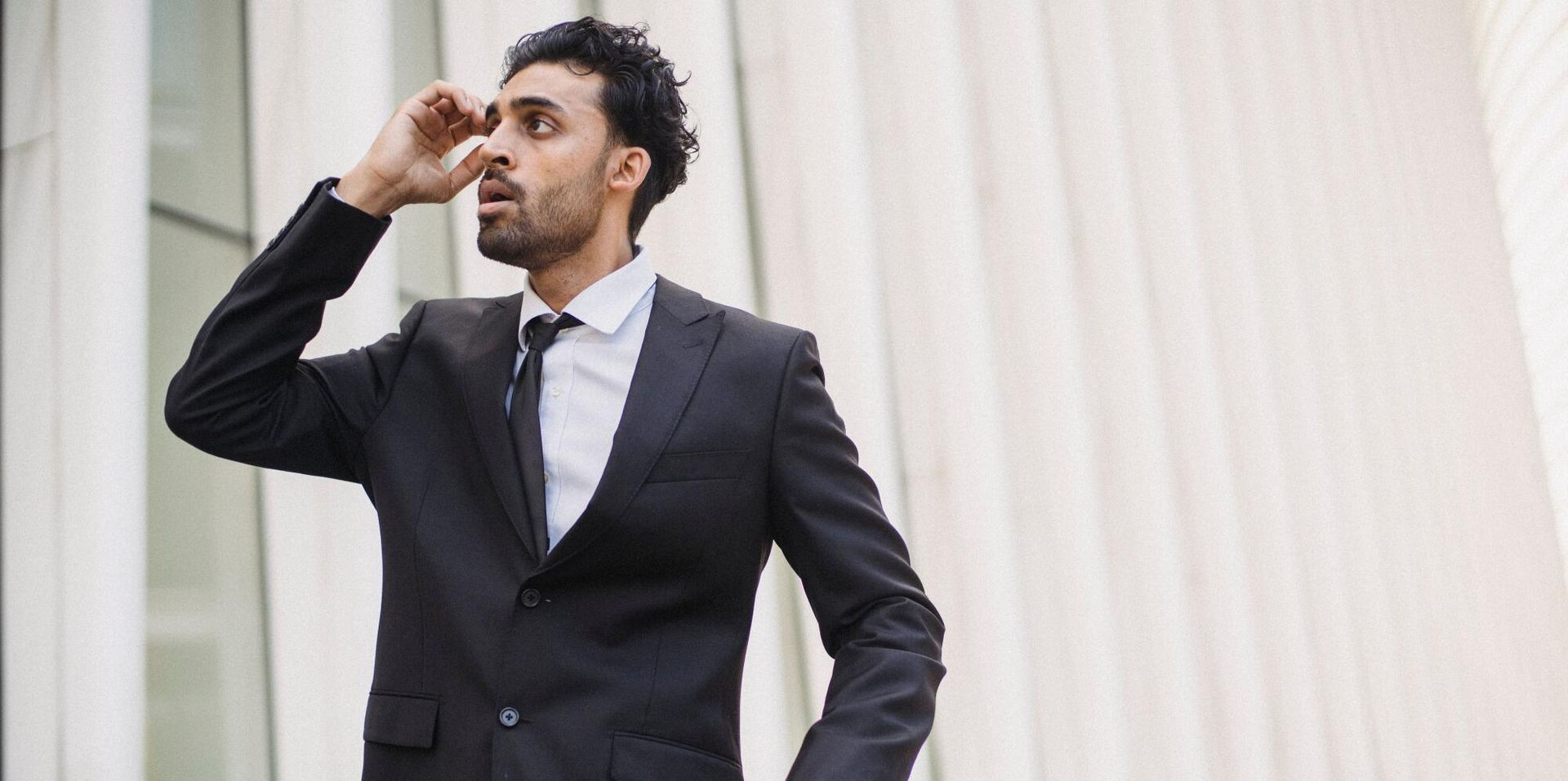 Man in a black suit holding a briefcase and looking into the distance outside a building