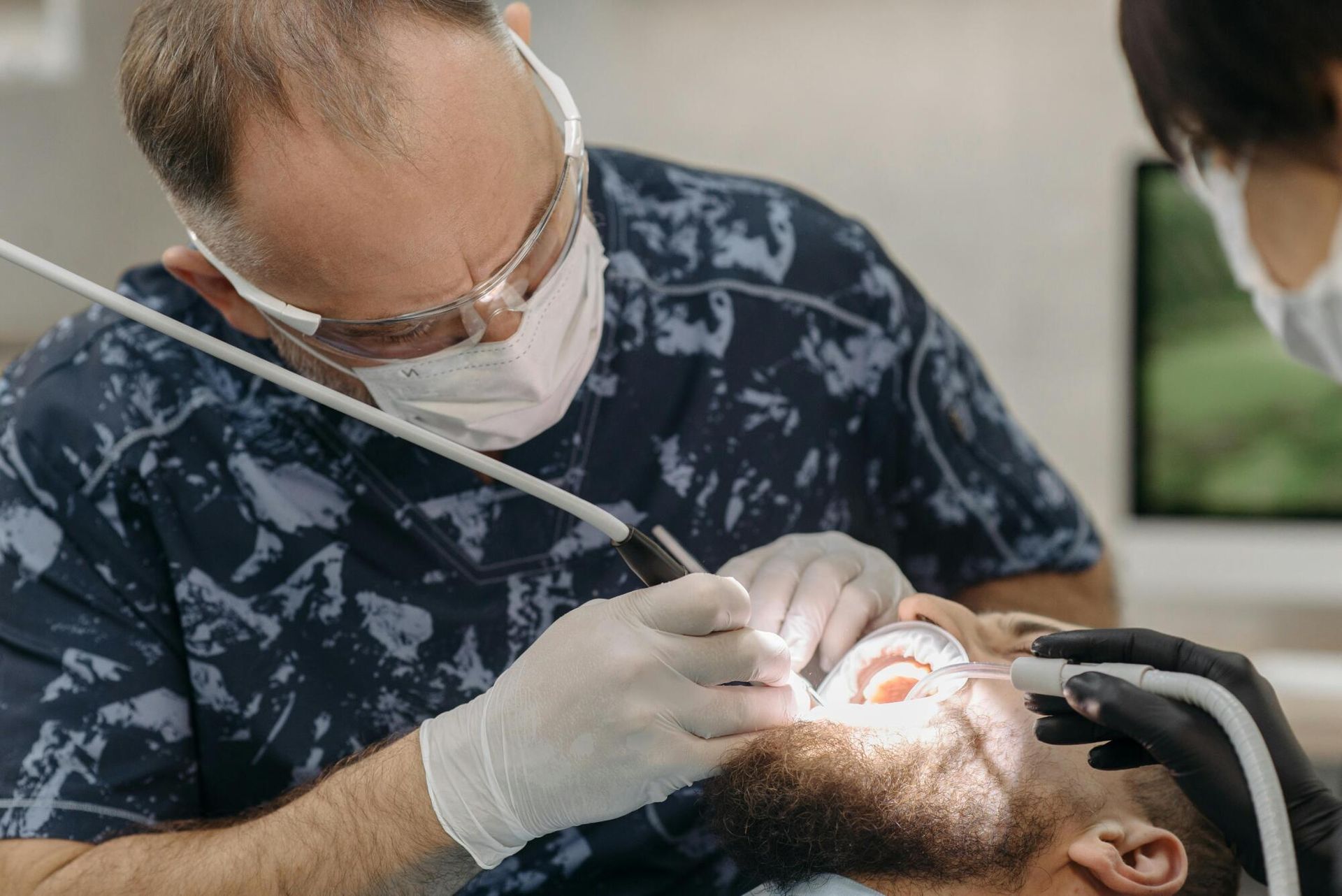 Dentist wearing mask and gloves treats a patient’s teeth with a bright dental light.