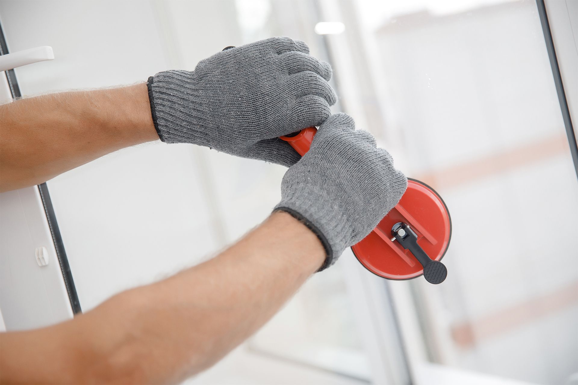 Gloved hands using a red paint roller on a white wall.