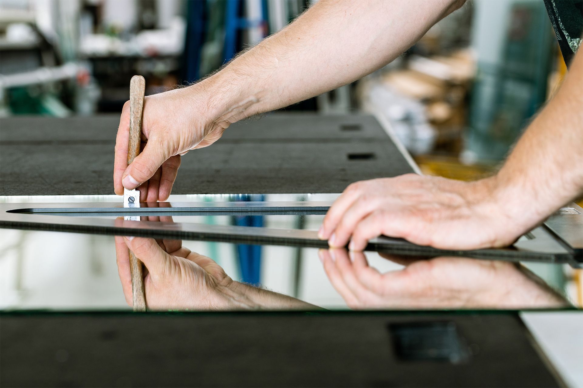 Hands aligning metal rods on a reflective glass surface in a workshop.